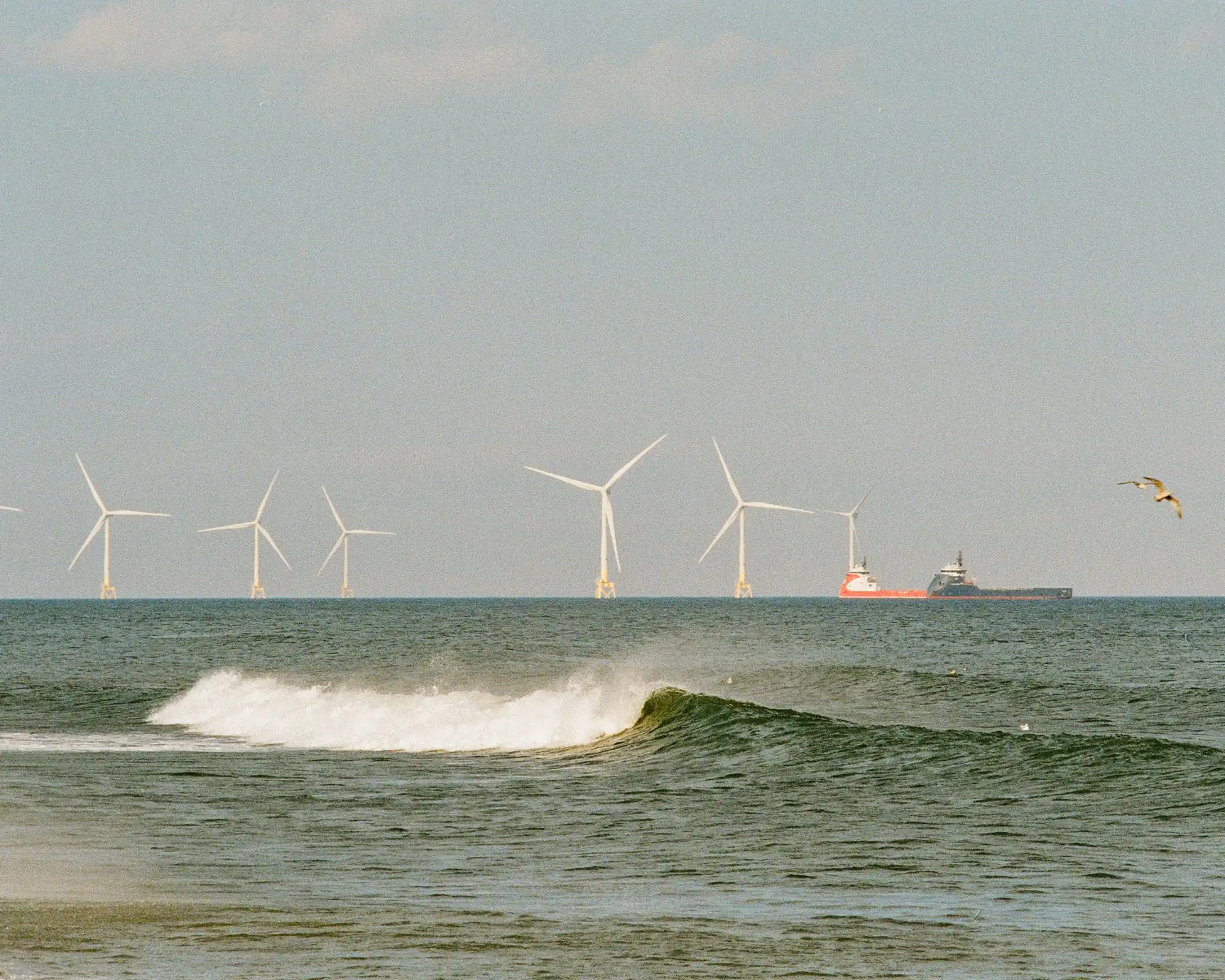 Des éoliennes en mer et un navire de ravitaillement au large d'Aberdeen, vus depuis la plage, avec une vague qui déferle au premier plan. Photographie d'archive prise sur la côte d'Aberdeen, pas à Cove Bay.